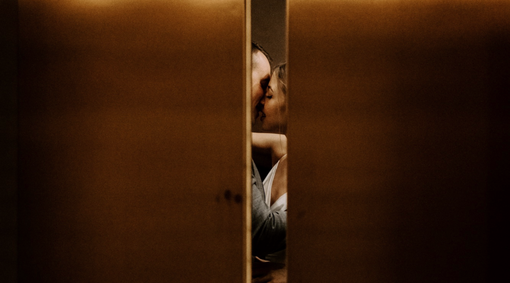 Bride and groom sharing a kiss between wooden doors in warm amber light