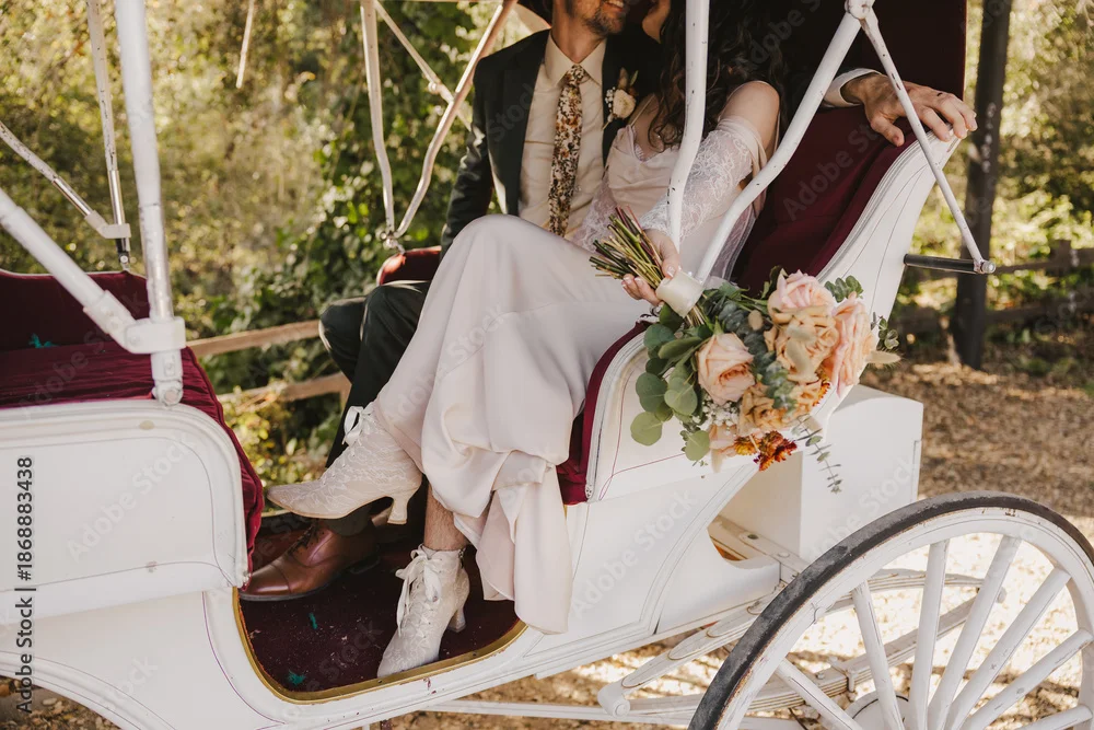 Bride and groom sitting together in a vintage white carriage holding a bouquet