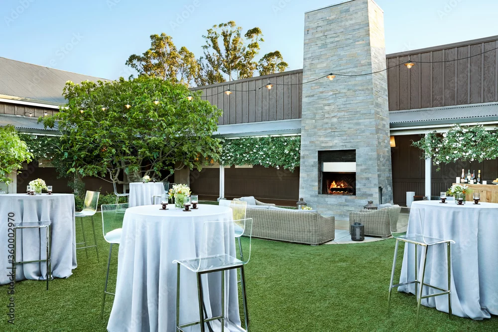 Outdoor cocktail reception area with high-top tables, string lights and a stone fireplace