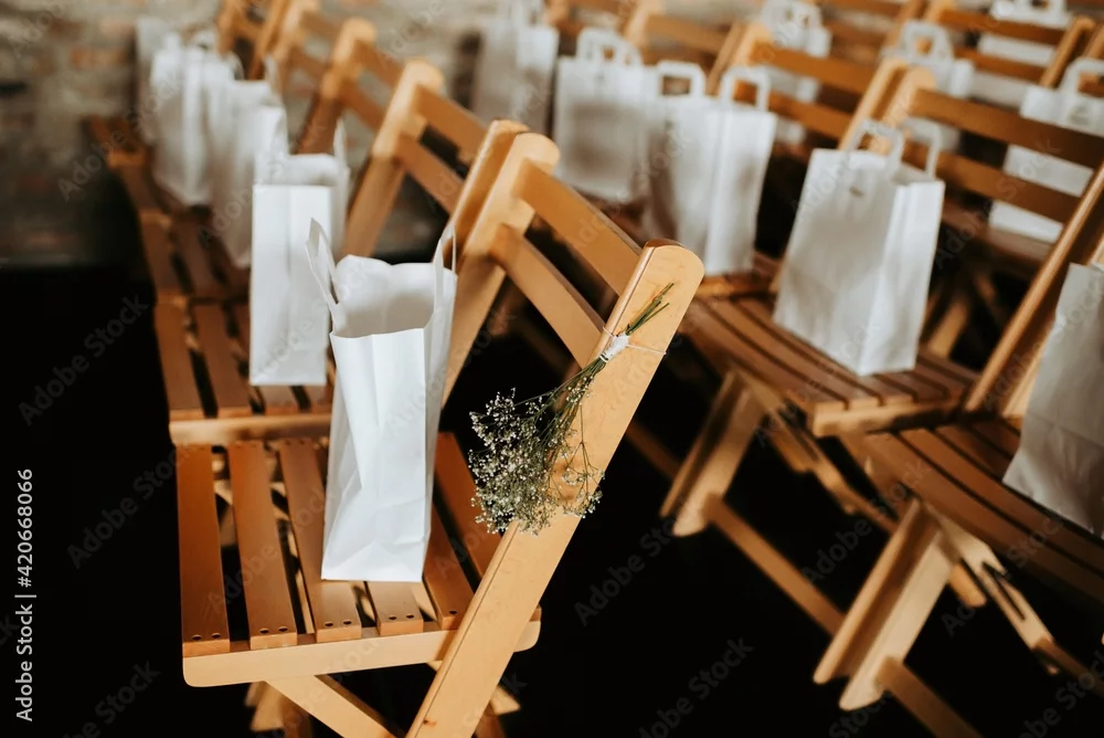 Rows of wooden chairs with white favor bags and sprigs of baby's breath