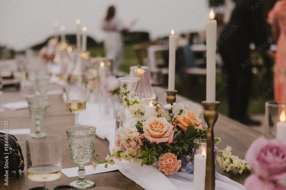 Reception table with lit candles, peach roses and vintage glassware at dusk