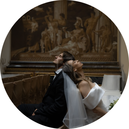 Circular portrait of a bride and groom looking upward in front of an ornate mural