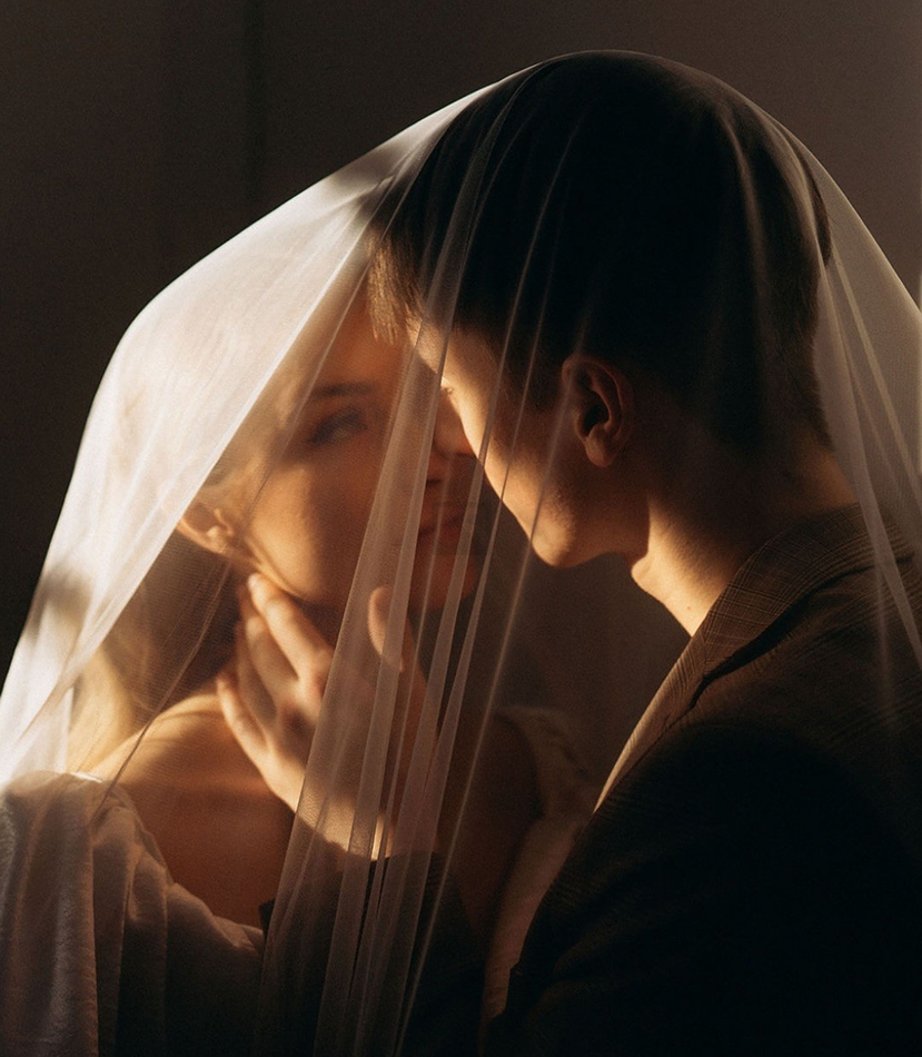 Bride and groom embracing under a sheer veil in soft sunlight
