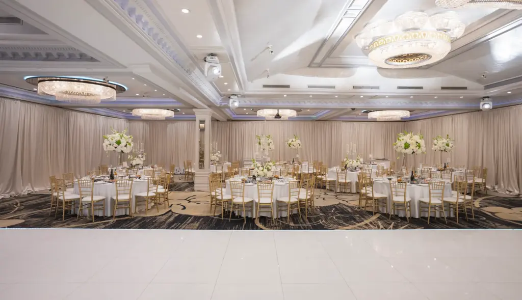 Glenoaks Ballroom reception setup with round tables, floral centerpieces and a draped backdrop