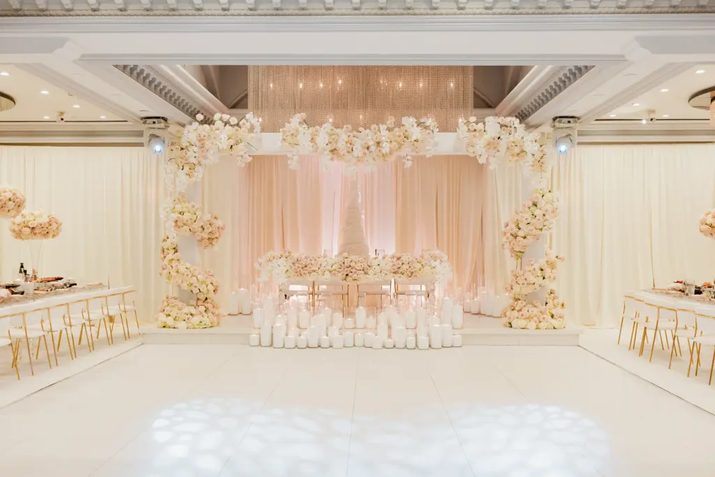Glenoaks Ballroom reception stage with a white floral arch and rows of candles