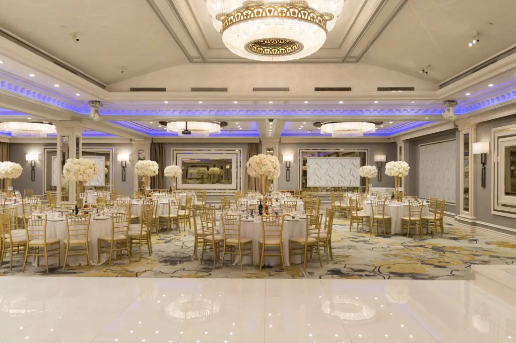 Wide view of the Glenoaks Ballroom set with round tables, gold chiavari chairs and blue lighting