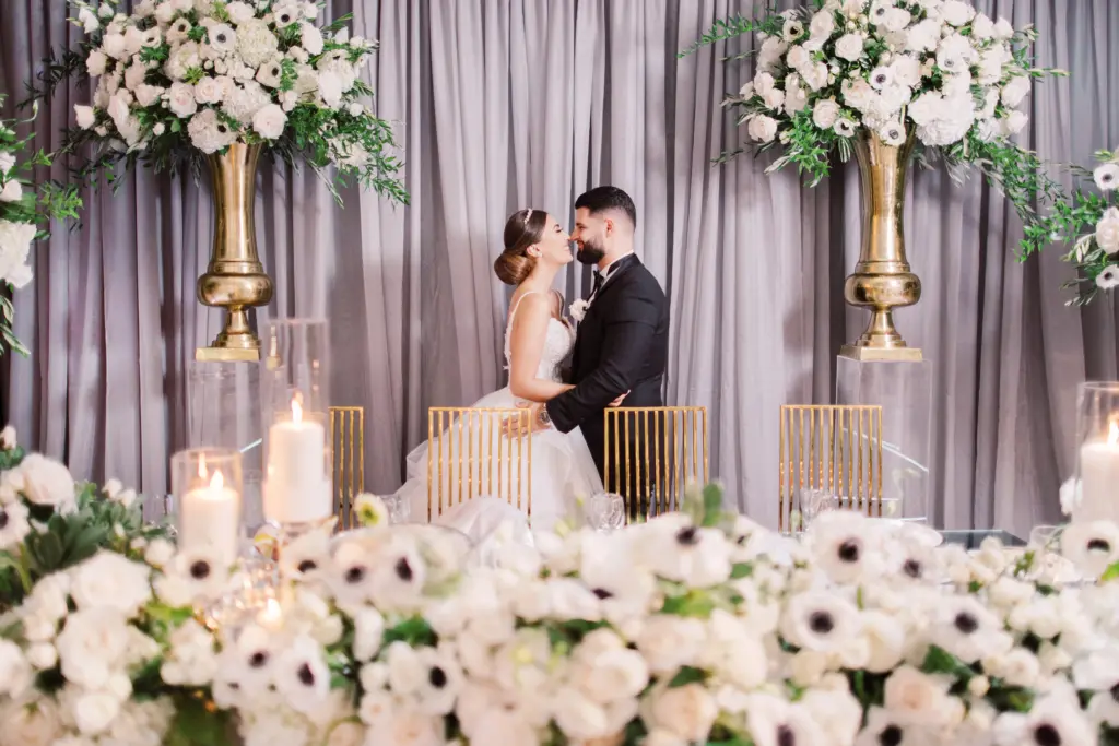 Bride and groom sharing a kiss on stage between tall white floral arrangements at Glenoaks Ballroom