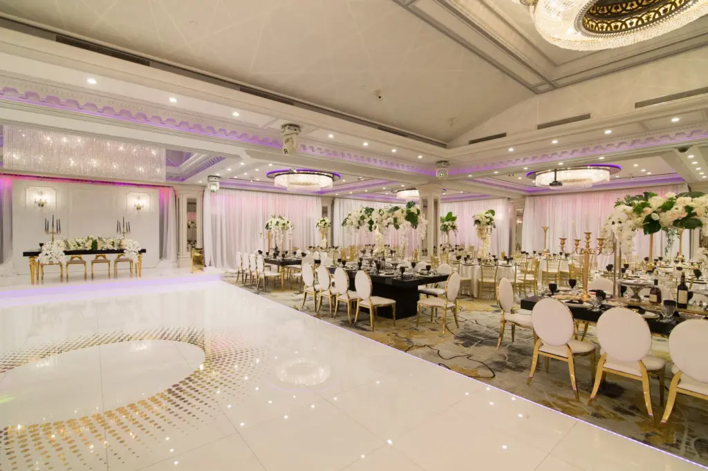Glenoaks Ballroom reception with black-linen tables and gold chairs beside a glossy white dance floor