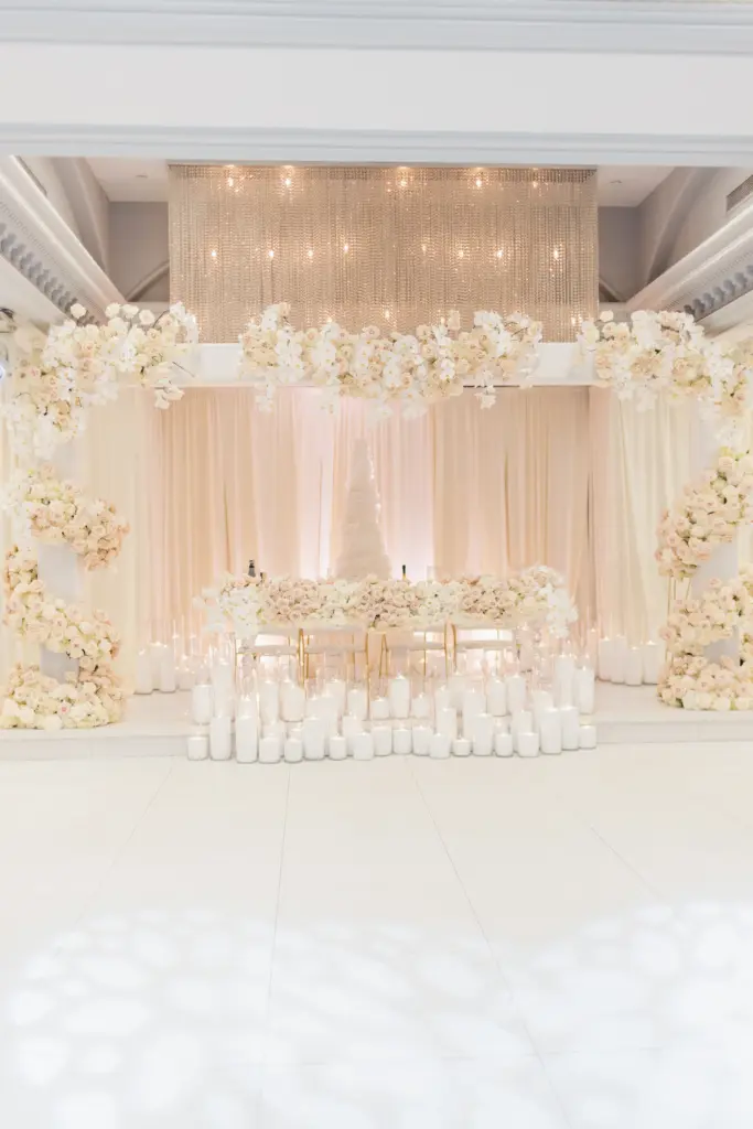 Floral arch with candles over a sweetheart table and tiered wedding cake at Glenoaks Ballroom