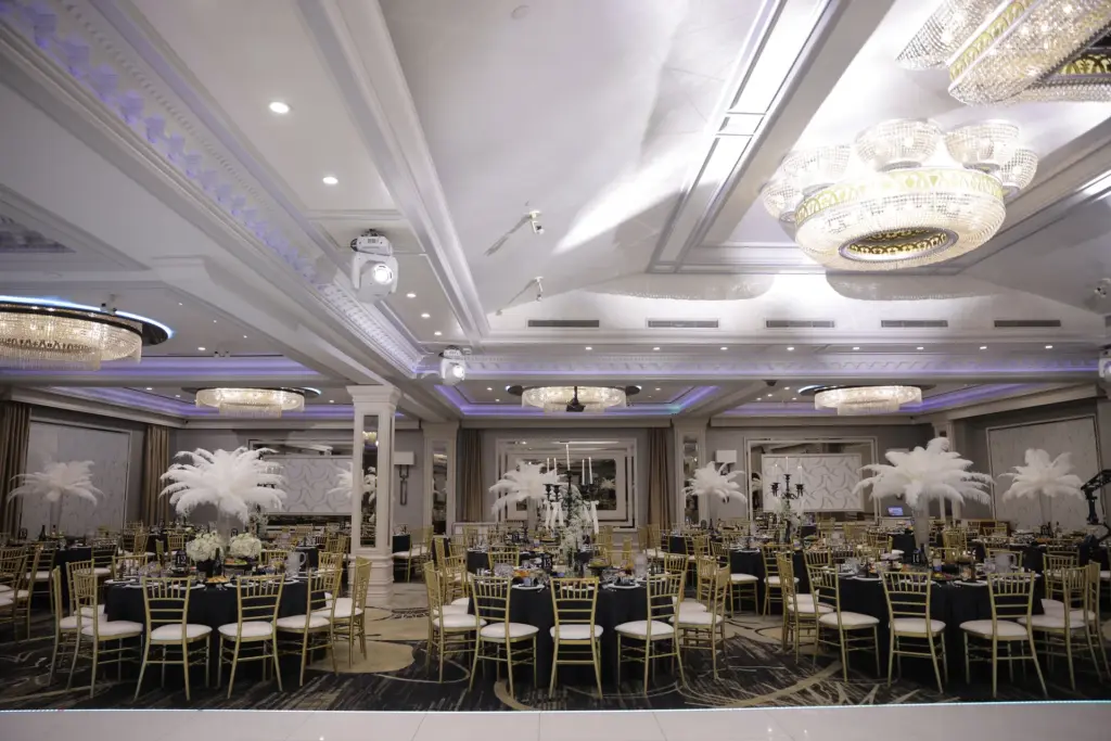Art deco-style ballroom set with black tablecloths, gold chairs and white ostrich feather centerpieces