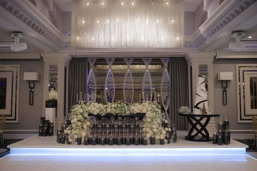Sweetheart table backdrop with mirrored panels, white floral arrangement and rows of candles