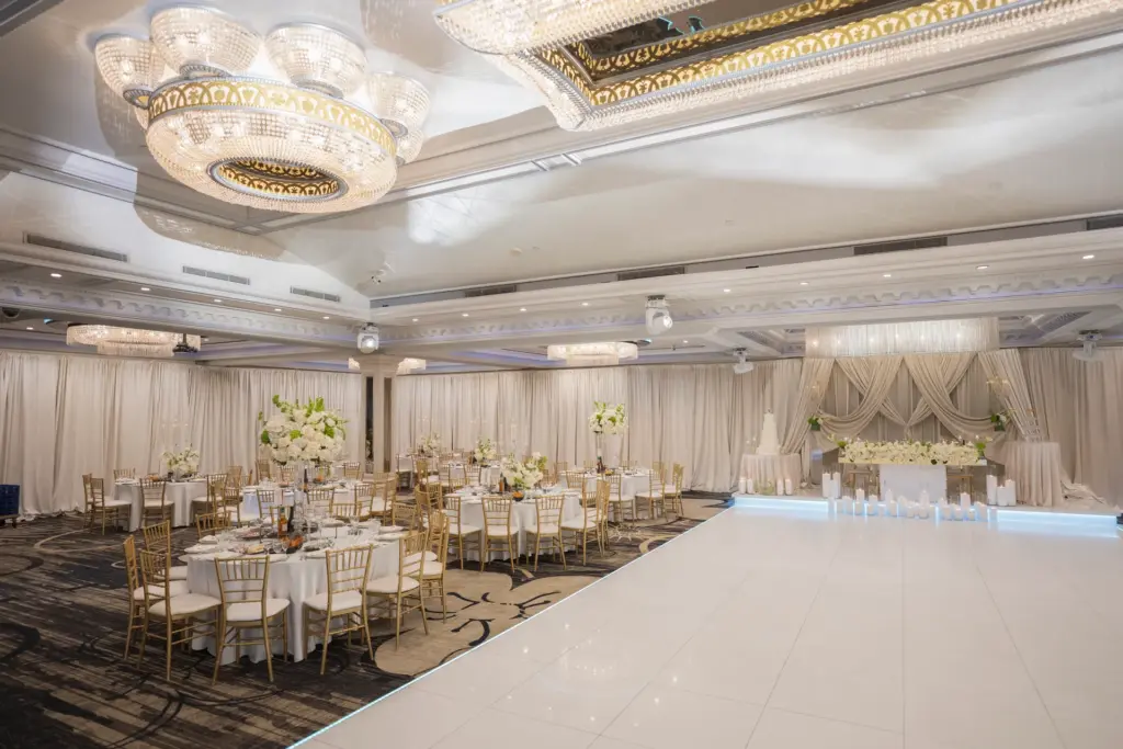 Ballroom reception with round tables, gold chairs and a draped sweetheart table backdrop