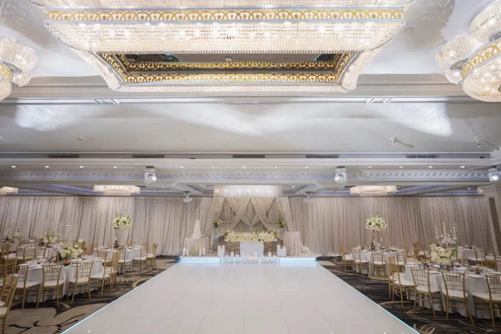 Ballroom dance floor leading to a draped cream backdrop with cake table and floral display