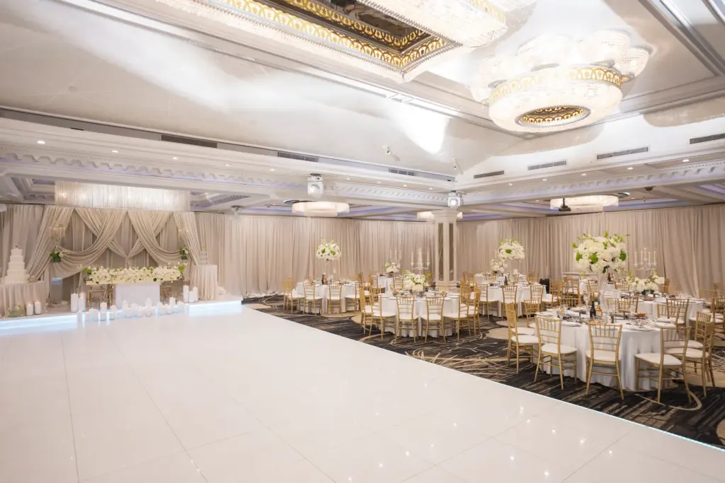 Ballroom set with cream drapery, round white-linen tables and a tiered cake display
