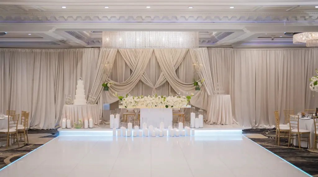 Ballroom reception with draped stage backdrop, wedding cake and gold chiavari chairs