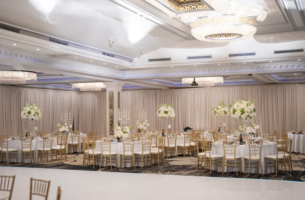 Wide view of ballroom set for a wedding with a sweetheart table backdrop and dinner tables