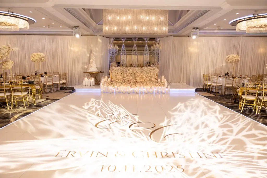 White dance floor illuminated with a couple's monogram and date projection beside a floral backdrop
