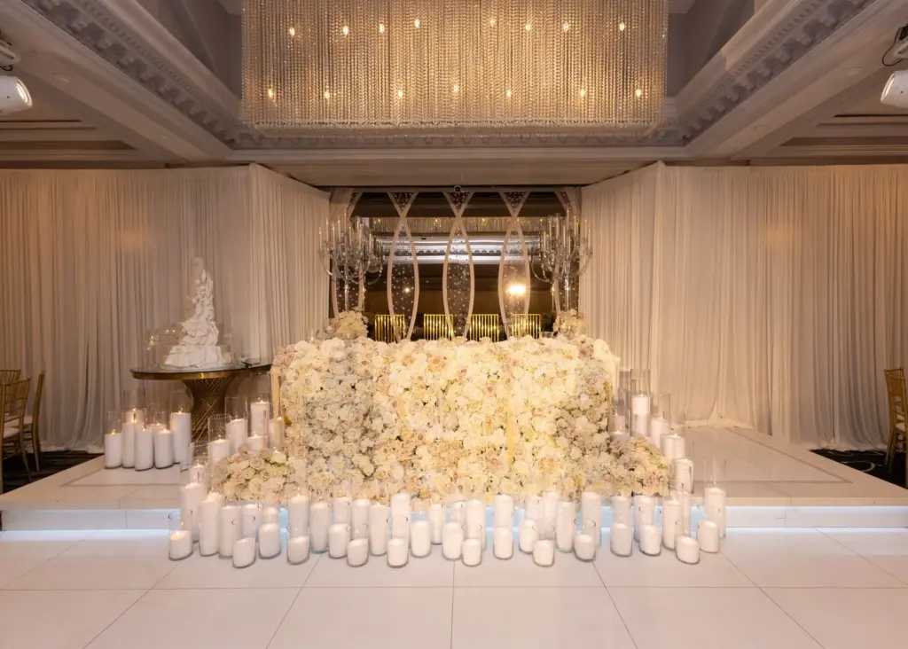 Floral-covered riser with rows of candles, a crystal chandelier and a tiered wedding cake