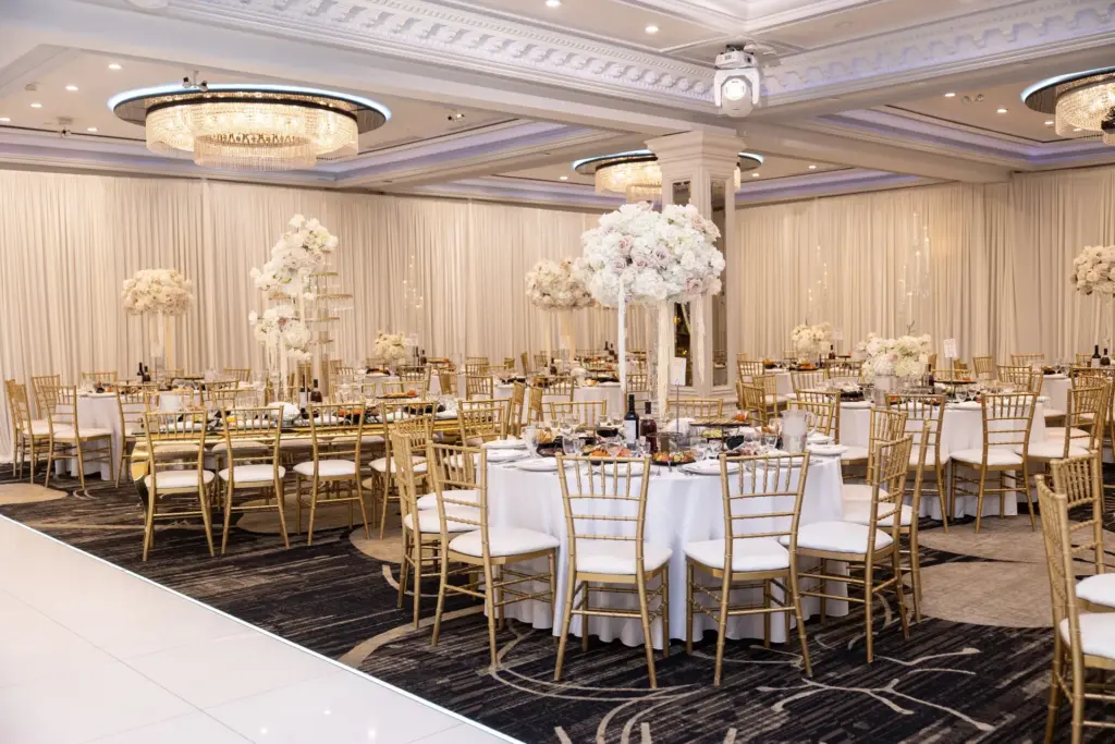 Ballroom reception with tall floral centerpieces and gold chiavari chairs around round tables