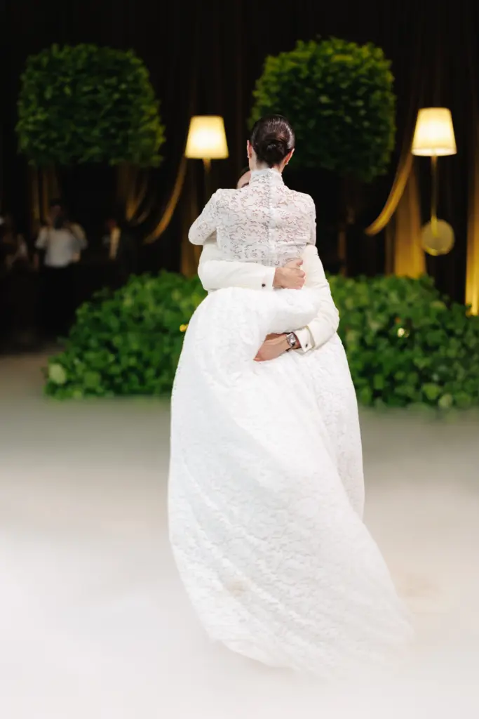 Rear view of bride and groom dancing embrace with a lace gown train flowing across the floor