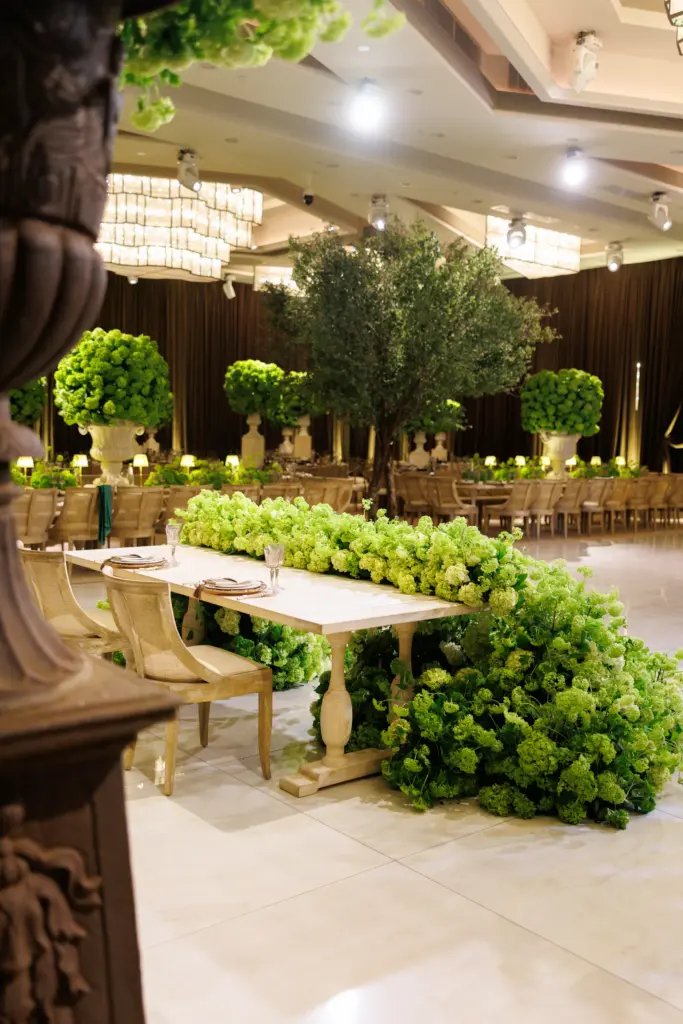 Banquet table draped in cascading green floral garland beneath an indoor olive tree