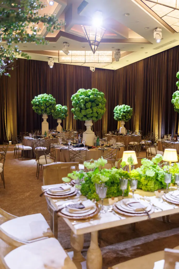 Wide view of round and banquet tables with topiary trees in The Landmark ballroom
