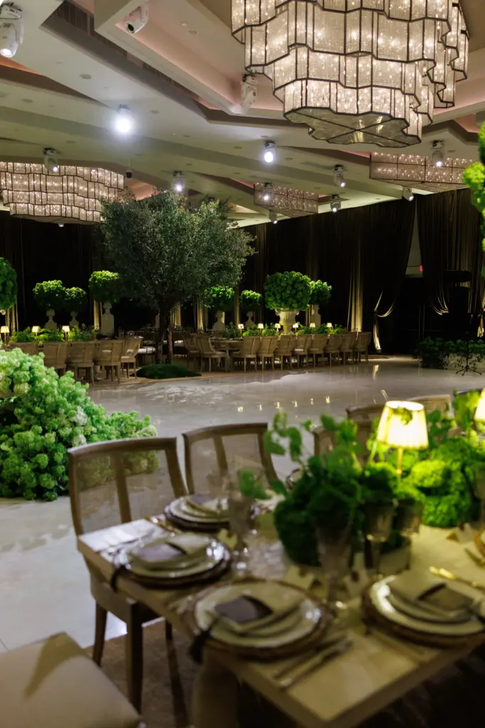 Tall green topiary urns and a floral arrangement on the ceremony stage, cake in the background