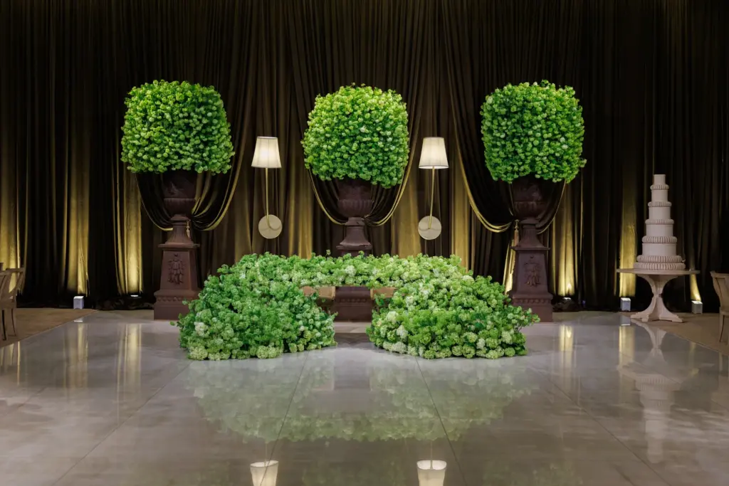 Bride and groom standing behind a lush floral wall on the ceremony stage