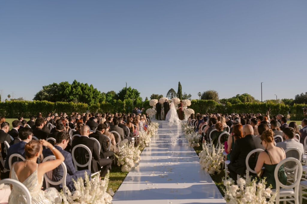 Wedding guests seated outdoors near The Landmark's tower and pergola on a sunny day