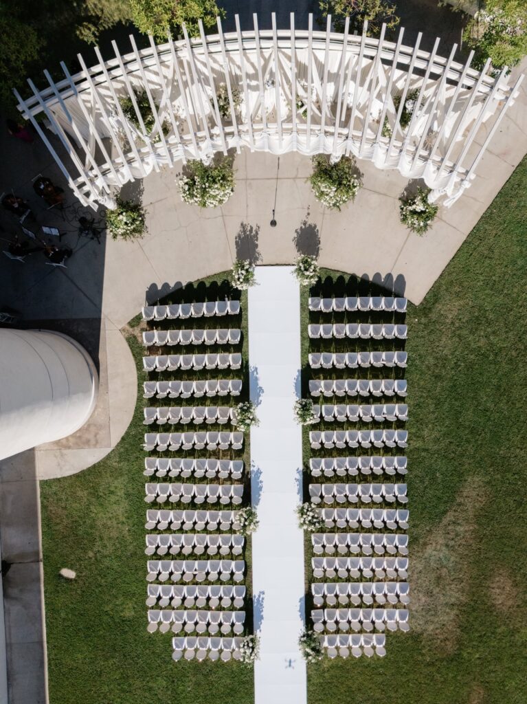 Black and white aerial close-up of ceremony chairs and a floral-lined aisle