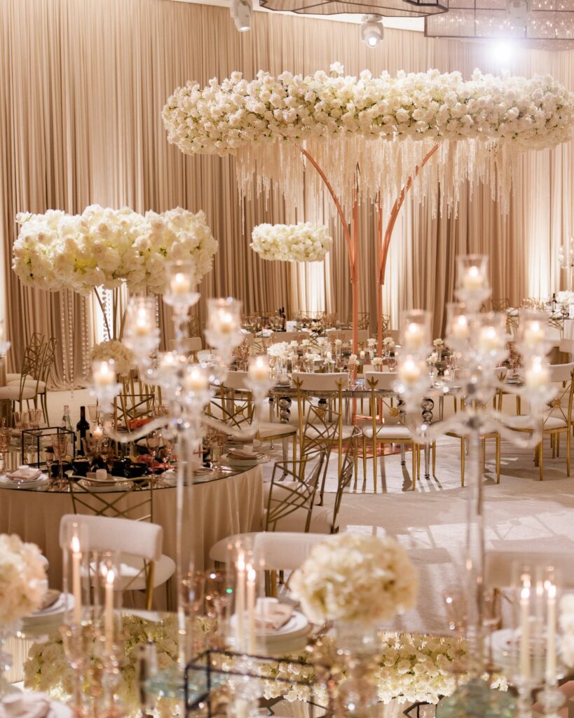 Suspended white floral cloud centerpiece with hanging strands above candlelit reception tables