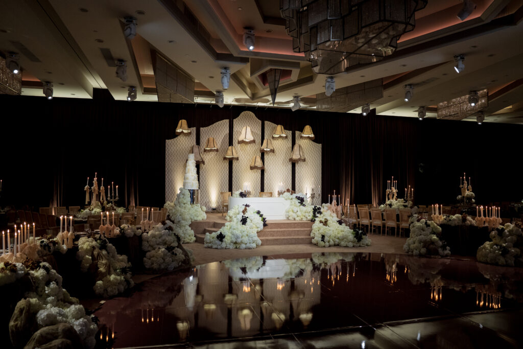 Wedding reception ballroom with a tiered cake, floral stage, and long candlelit guest tables