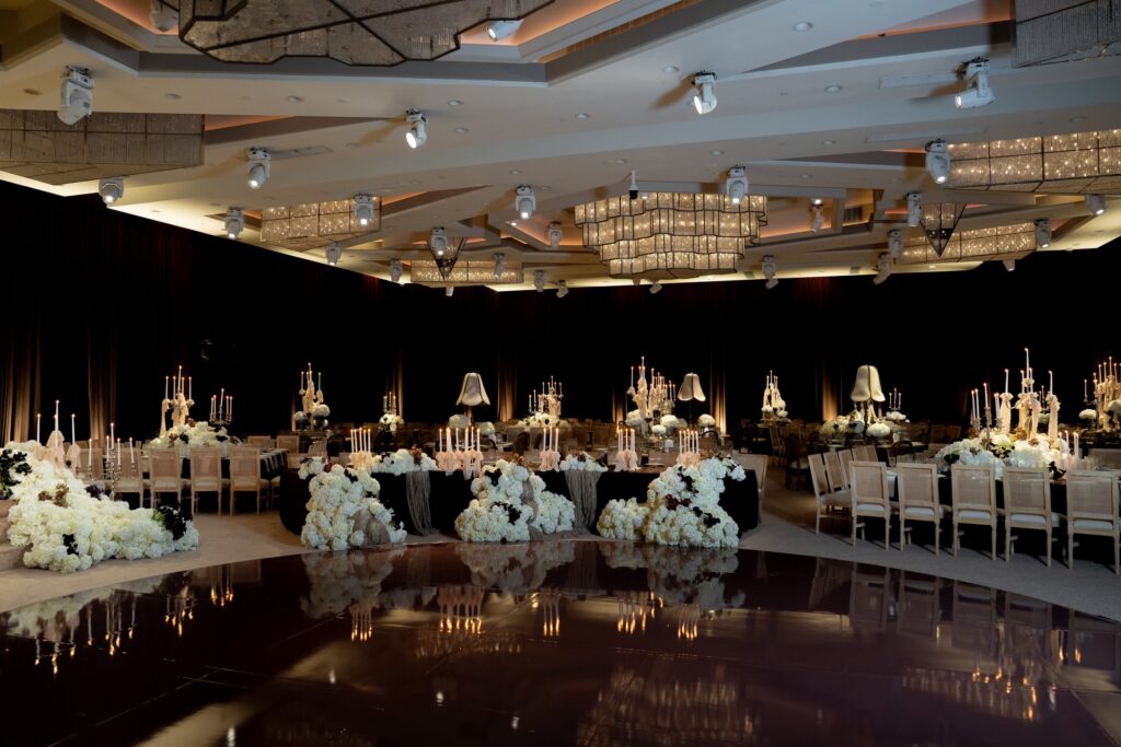 Reception ballroom with black-linen tables, floral clusters, and layered crystal chandeliers