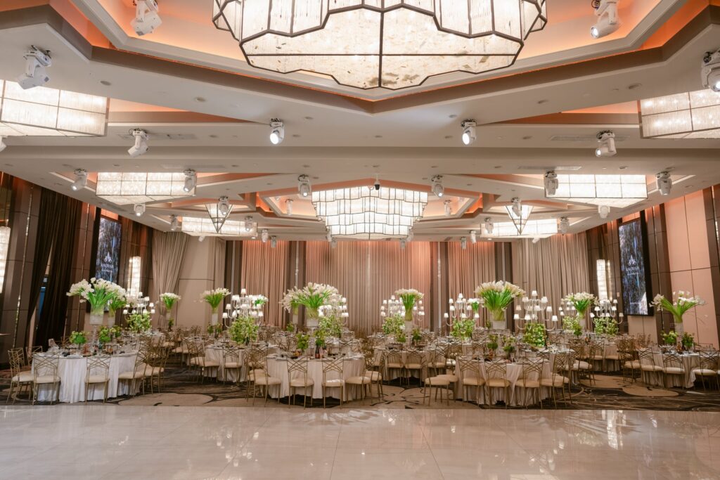 Ballroom reception with a center aisle of tall white lily arrangements under sculptural chandeliers