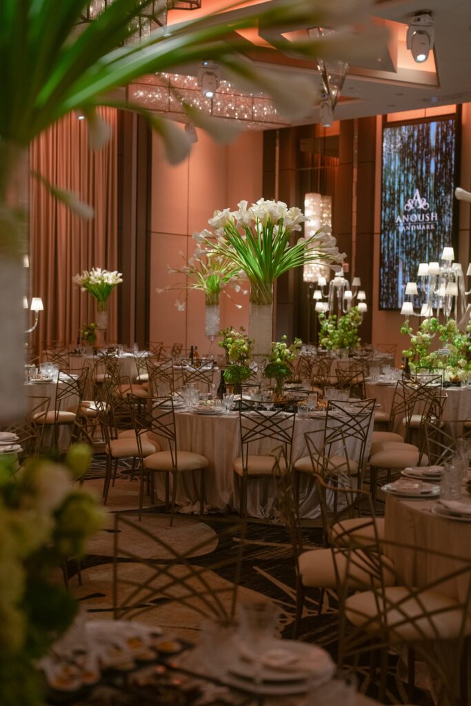 Reception table with a tall lily centerpiece in front of an illuminated Anoush Landmark sign