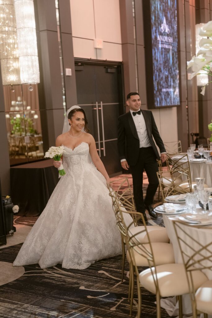 Bride and groom entering their reception past a lit Anoush Landmark sign and set tables