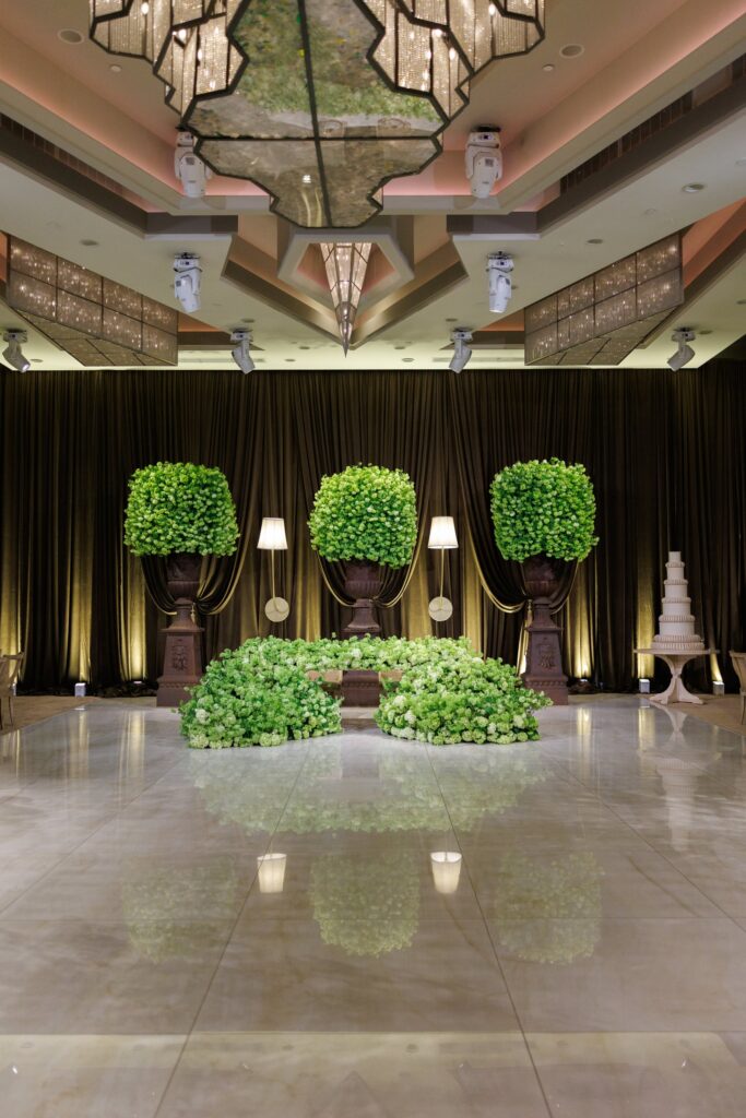 Sweetheart table flanked by three green hydrangea topiary trees under a mirrored ceiling