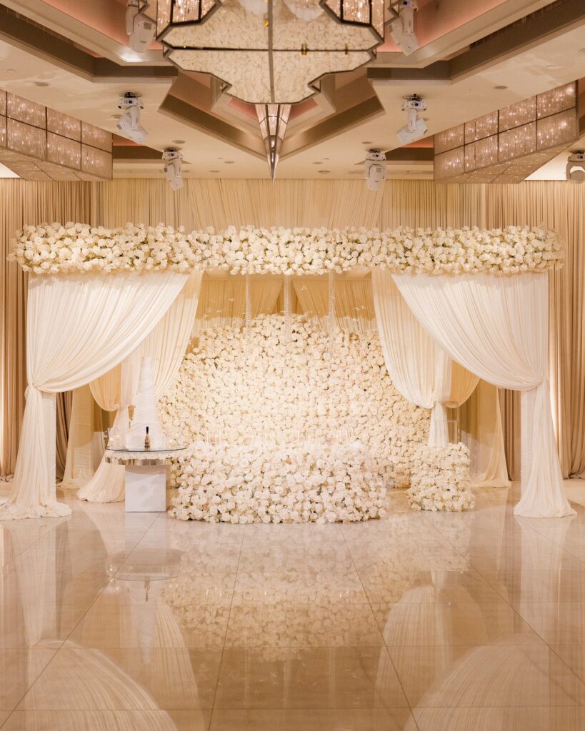 White rose-covered canopy backdrop draped over a cake table on a marble floor