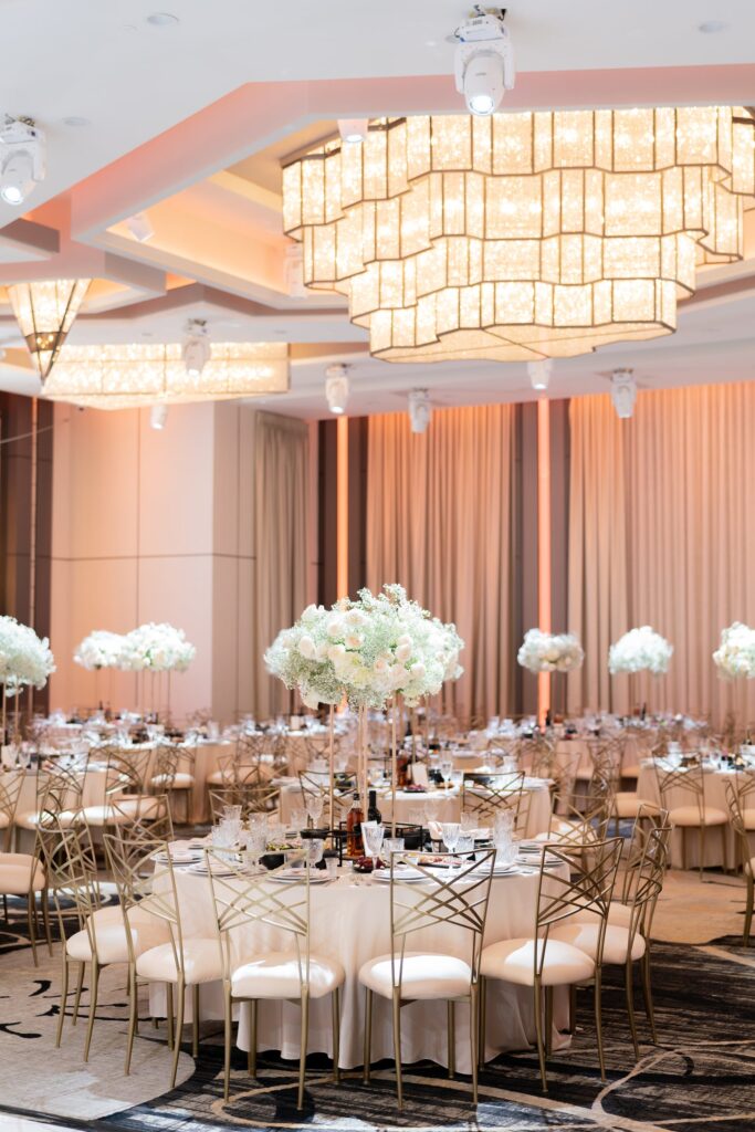 Round reception tables with tall white rose and baby's-breath centerpieces under crystal chandeliers