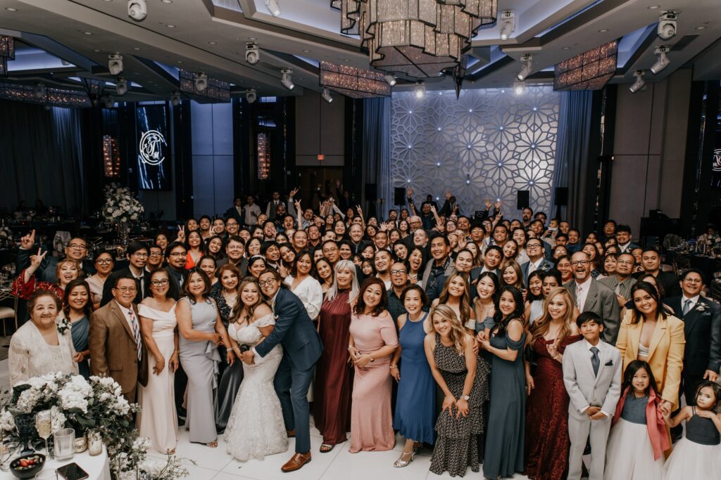 Large wedding party and family group photo posed in a ballroom reception hall