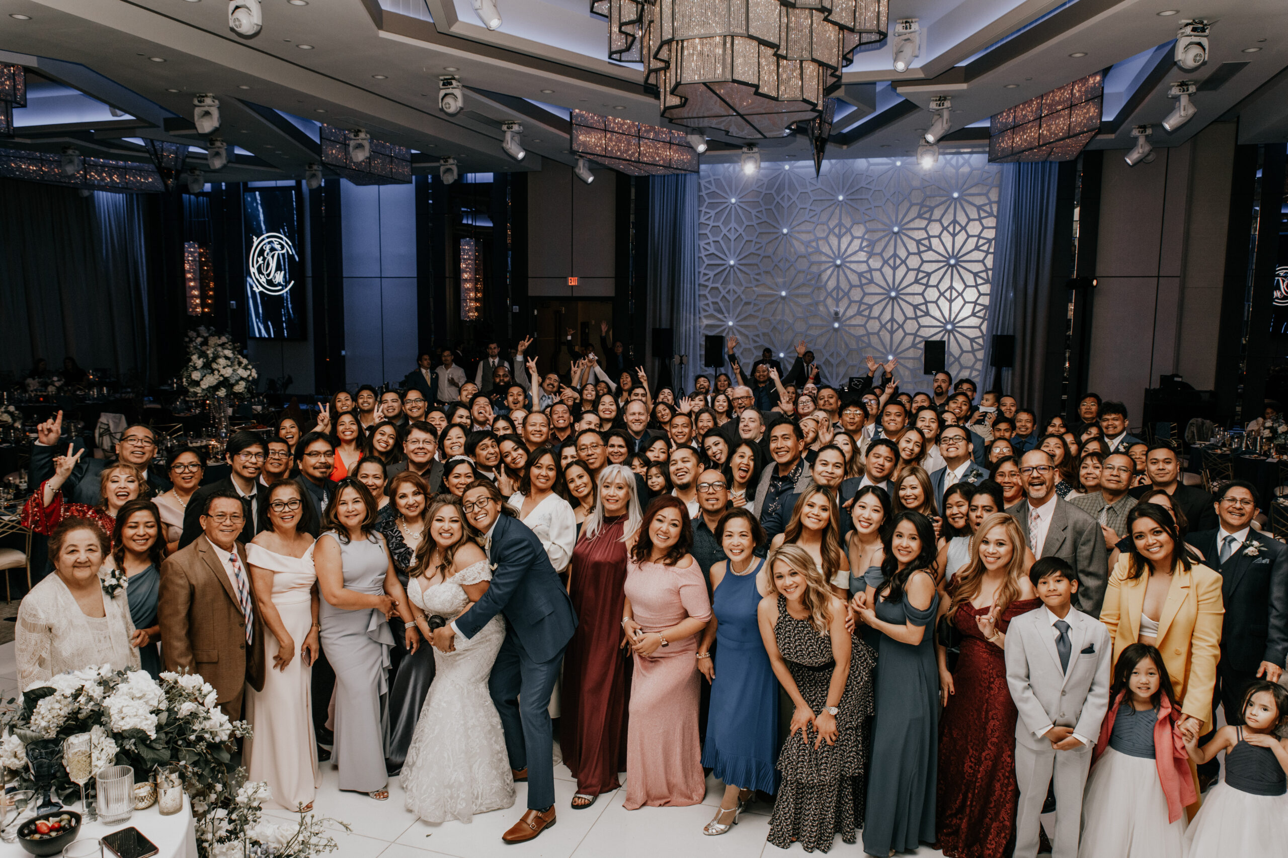 Wedding guests and family gather for a large group portrait in a ballroom reception hall