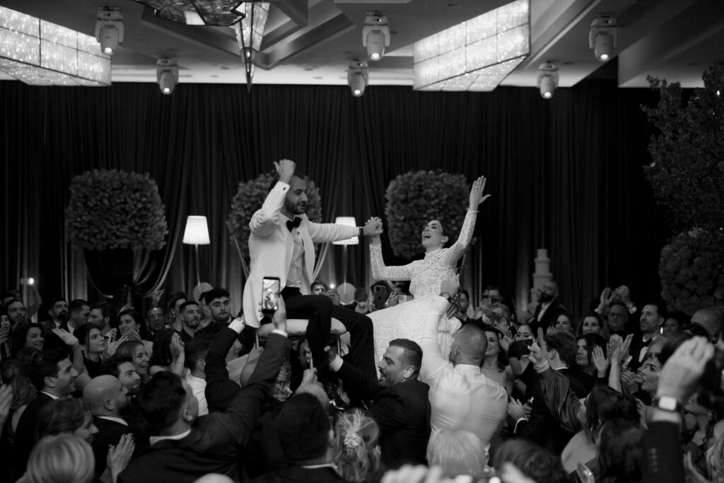 Black-and-white photo of guests lifting the bride and groom during the reception celebration