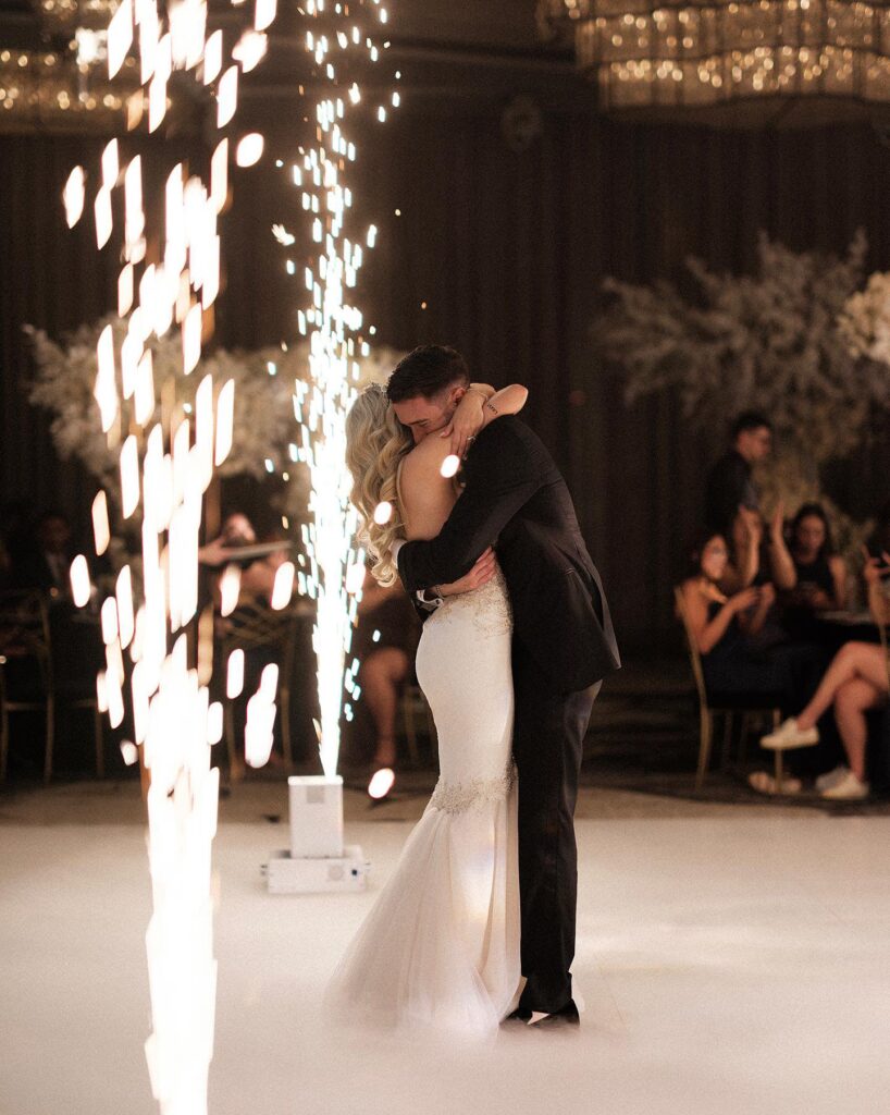 Bride and groom share a first dance beside a cold-spark fountain on a white dance floor