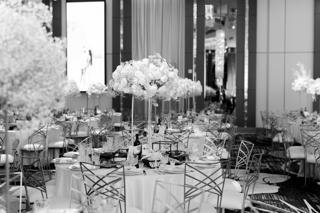 Black-and-white photo of round reception tables with tall white floral centerpieces
