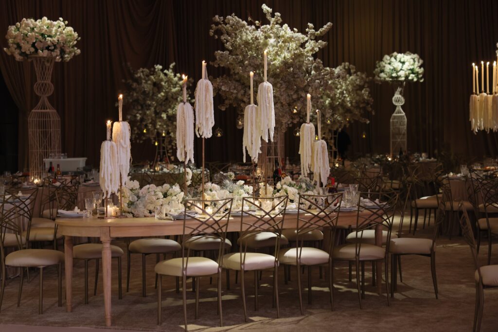 Long wooden banquet table with a white floral runner and hanging tassel-topped candle stands