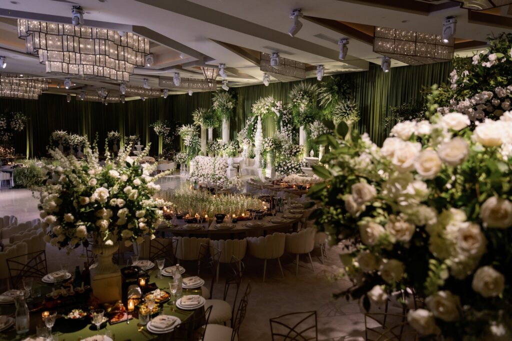 Reception ballroom with green drapery, a white floral archway, and rose centerpieces on tables