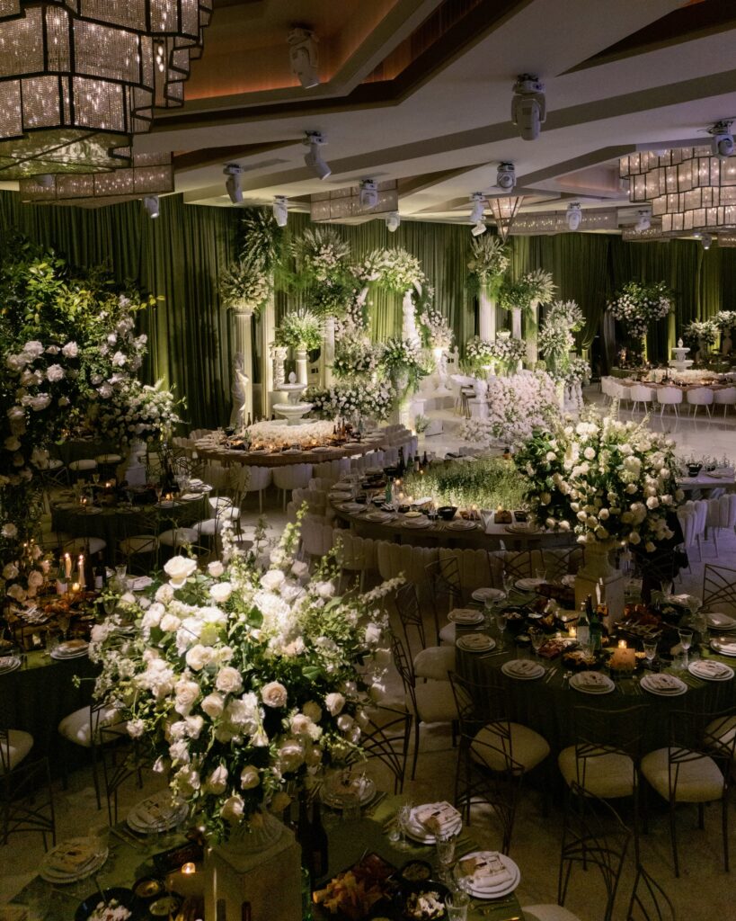 Green-draped ballroom with a floral column archway and round tables set for a reception