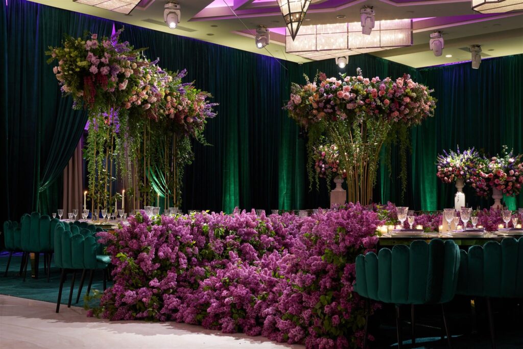 Long table with a lilac floral runner and hanging pink floral clusters under green drapery