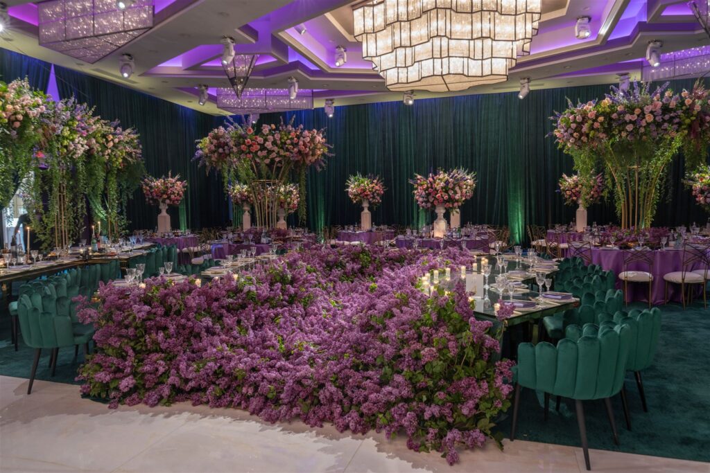 Reception hall with a lilac floral table runner and tall pink centerpieces under purple lighting