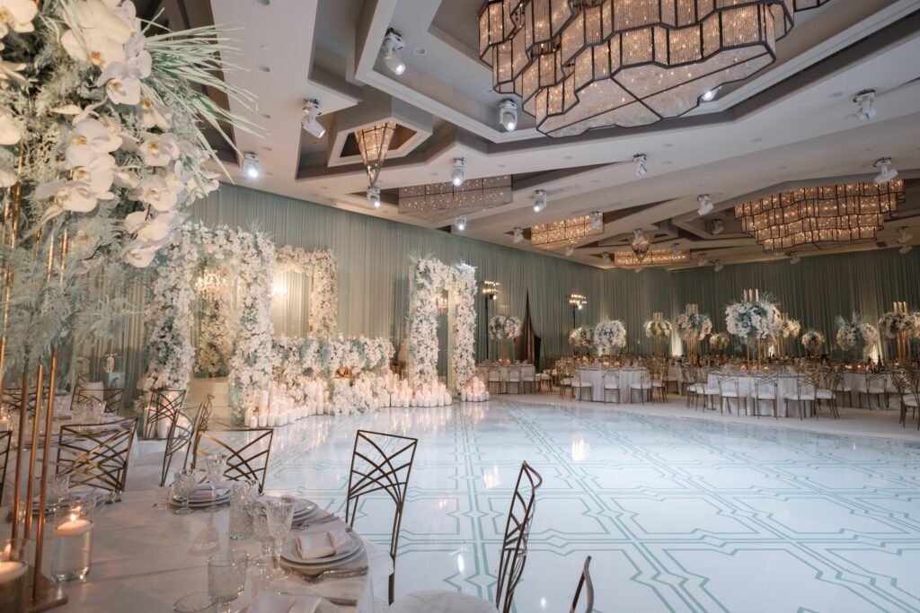 Ballroom with a white floral archway and a mint-green patterned dance floor for a reception